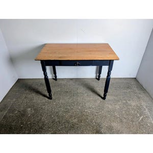 Puede incluir: Una mesa rectangular de madera con tapa de madera natural y base pintada de negro. La mesa tiene un solo cajón y cuatro patas torneadas. La mesa mide aproximadamente 91 cm de largo, 61 cm de ancho y 76 cm de alto.