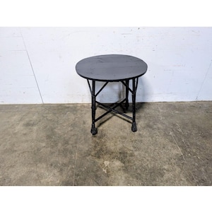 Puede incluir: Una pequeña mesa redonda negra con un acabado oscuro. La mesa tiene una base decorativa con soportes entrecruzados y patas ornamentadas. La mesa tiene aproximadamente 61 cm de diámetro y 51 cm de alto, adecuada para espacios pequeños.