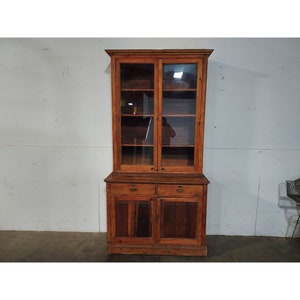 May include: A vintage wooden cabinet with glass doors and two drawers. The cabinet has a dark brown stain and is in good condition.