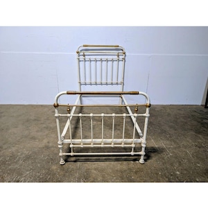May include: An antique white metal bed frame with brass accents. The headboard and footboard feature vertical bars and decorative brass finials. The bed frame has rounded corners and a classic, vintage aesthetic.