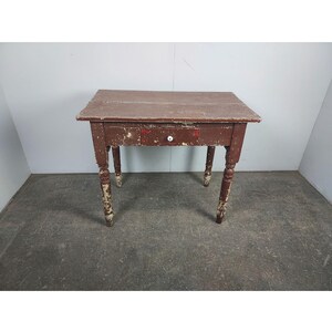 May include: A brown wooden table with a single drawer and turned legs. The table has a distressed finish and shows signs of wear.