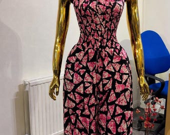 Könnte beinhalten: Ein ärmelloser Jumpsuit mit Neckholder-Ausschnitt und gesmoktem Oberteil. Das Kleidungsstück ist mit einem geometrischen Muster aus rosa und weißen Dreiecksformen auf schwarzem Grund verziert und hat eine weit geschnittene Hose.