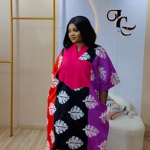 K&ouml;nnte beinhalten: Ein locker sitzendes Kaftan-Kleid mit einem lebendigen Color-Block-Design in Rot, Schwarz und Lila. Das Kleidungsst&uuml;ck hat einen V-Ausschnitt, kurze &Auml;rmel und ein sich wiederholendes wei&szlig;es Blattmuster auf den schwarzen und lila Stoffteilen.