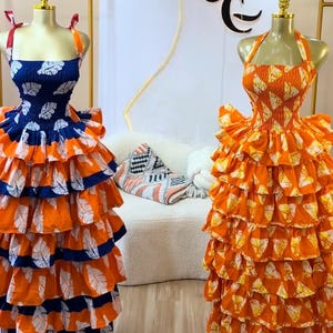 Peut inclure: Deux robes sans manches sur mannequins. La robe de gauche présente un corsage bleu à motifs de feuilles blanches et des étages à volants orange. La robe de droite est entièrement orange avec des motifs de feuilles blanches et des volants.