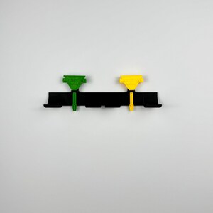 May include: A black plastic mounting bracket with two colored clips. One clip is green with the text "MORE DAY" and the other is yellow. The clips are attached to the bracket with a vertical post.