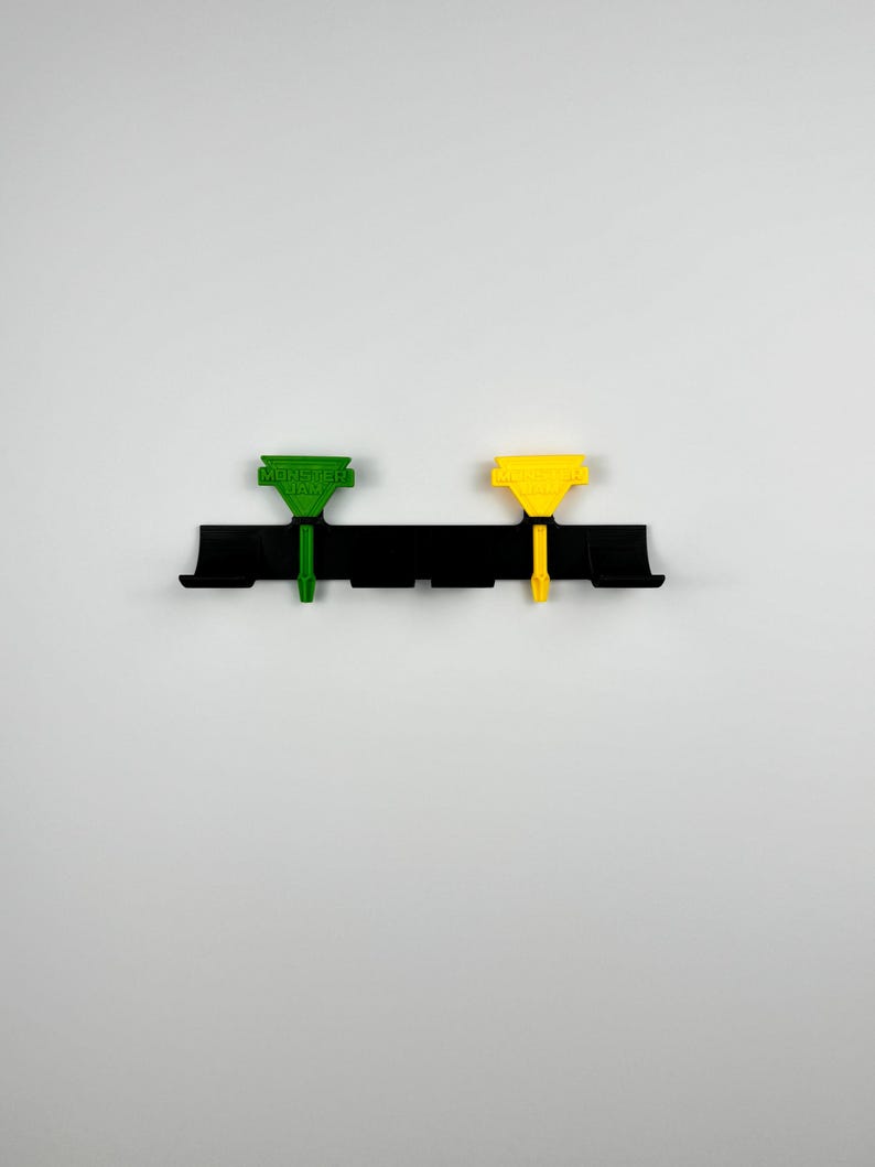 May include: A black plastic mounting bracket with two colored clips. One clip is green with the text "MORE DAY" and the other is yellow. The clips are attached to the bracket with a vertical post.