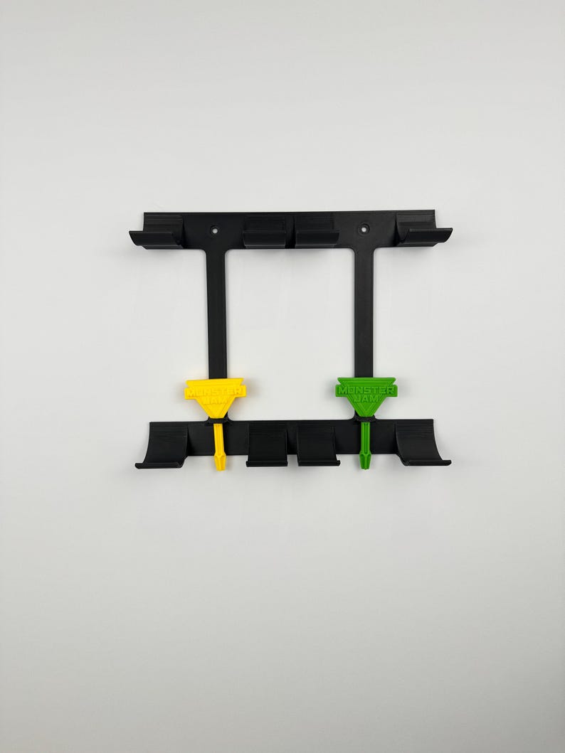 May include: Black wall-mounted tool holder with two colored tools. The holder has multiple slots and a rectangular frame. One tool is yellow, the other is green, both with text. The background is white.