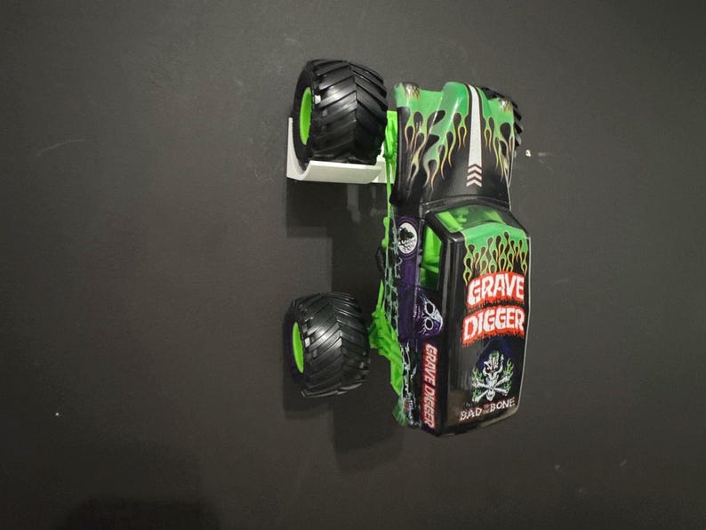 May include: A toy monster truck in green and black, featuring the words "Grave Digger" and a skull graphic. The truck has large black tires with green accents and a flame design.