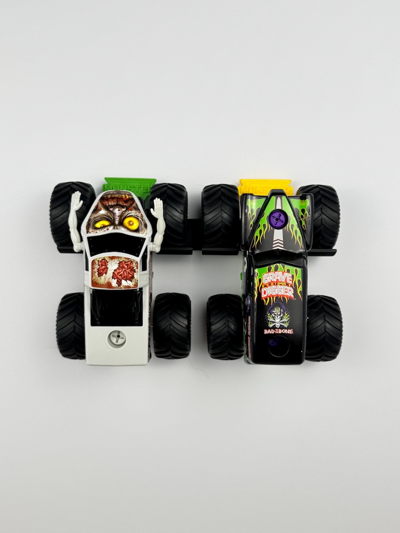 May include: Two toy monster trucks, one white with a zombie face and the other black with "Grave Digger" and "Bad Bone" graphics. Both have large black tires and are set against a white background.