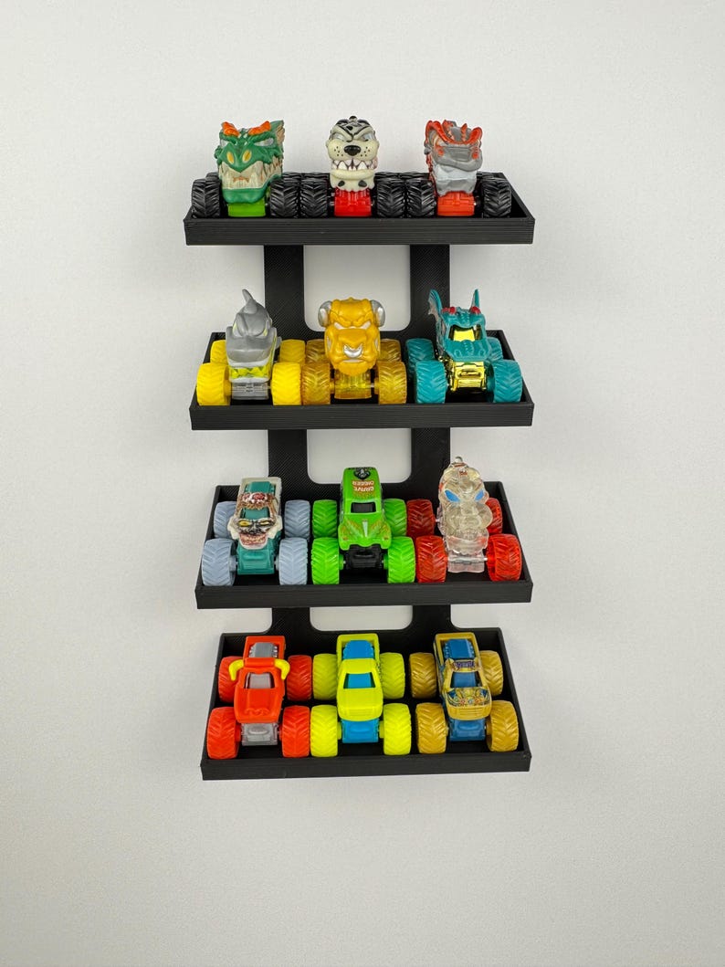 May include: A black wall-mounted shelf unit displaying a collection of toy monster trucks. The trucks are various colors, including red, green, yellow, and blue. Each truck has large, oversized tires. The shelf unit has four tiers.