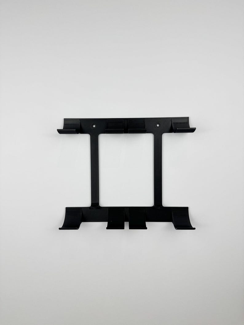 May include: Black metal wall-mounted organizer with a rectangular frame and multiple hooks. The organizer has a symmetrical design with two vertical supports and several horizontal bars for storage and display.