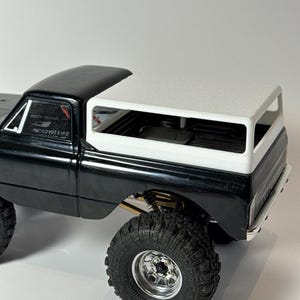 May include: Black and white model truck with large, knobby tires and chrome rims. The truck bed has a white top. The text "2-W-I 10A ESC/RX" is visible on the side of the truck.