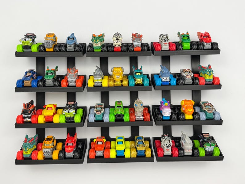 May include: A collection of colorful toy monster trucks displayed on black wall shelves. The trucks feature various designs and colors, including red, blue, green, and yellow. The shelves are mounted on a white wall.