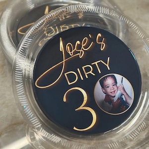 May include: Clear plastic coasters with a navy blue center featuring gold text that reads "Jose's DIRTY 30" and a small photo of a young boy. The coasters have a decorative edge.