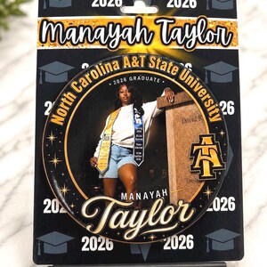 Op de afbeelding: Een afscheidscadeau met een foto van een afgestudeerde, Manayah Taylor, met de tekst "North Carolina A&T State University 2026 Graduate". Het ontwerp bevat het logo van de school en het jaar 2026.
