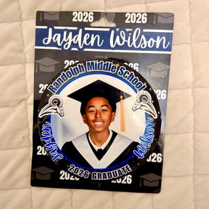 Könnte beinhalten: Ein Abschluss-Button mit einem Foto eines lächelnden jungen Menschen in Hut und Robe. Der Button enthält den Text "Randolph Middle School 2026 Graduate" und den Namen "Jayden Wilson."