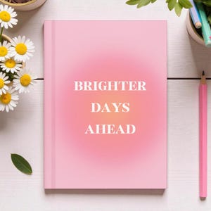 May include: A pink journal with the words "BRIGHTER DAYS AHEAD" in white. The journal is surrounded by daisies, a pink pencil, and other stationery items.