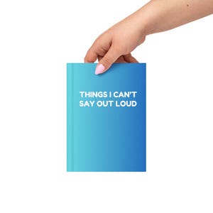 May include: A blue gradient notebook with the text "THINGS I CAN'T SAY OUT LOUD" in white. The notebook is held by a hand with pink nail polish.