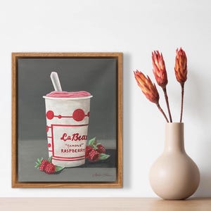 Puede incluir: Pintura enmarcada de un batido de frambuesa en un vaso blanco con detalles rojos y el texto "La Bear" y "Famous Raspberry". Hay frambuesas frescas en la base del vaso. Un jarrón con flores secas está a la derecha.