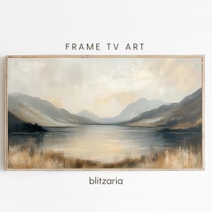Op de afbeelding: Een ingelijst landschapsschilderij met een serene meerzicht. Het kunstwerk toont gedempte tinten grijs, beige en bruin, met bergen, water en een bewolkte lucht. De tekst "FRAME TV ART" en "blitzaria" zijn zichtbaar.