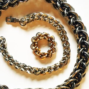 May include: Three silver chain necklaces of varying lengths, with a ring-shaped chain in the center. The chains are made of interlocking metal rings.