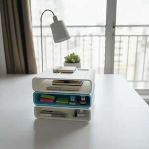 Puede incluir: Un organizador de escritorio de tres niveles en blanco y azul claro. El nivel superior contiene un cuaderno, un tel&eacute;fono y un bol&iacute;grafo. El nivel intermedio contiene notas adhesivas y una grapadora. El nivel inferior tiene bol&iacute;grafos y un recipiente peque&ntilde;o.
