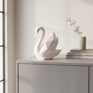 Könnte beinhalten: Eine weiße, geometrische Schwan-Skulptur mit modernem, kantigem Design. Der Schwan steht auf einem grauen Schrank, im Hintergrund eine Vase mit Blumen und Büchern. Die Skulptur ist ein dekoratives Wohnaccessoire.