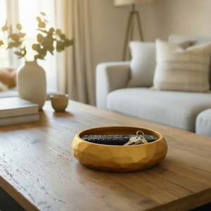 May include: A wooden coffee table with a gold-colored, faceted bowl holding a remote control and keys. A beige sofa and a dog are in the background. A vase with greenery and books are also on the table.