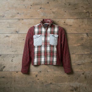 Pode incluir: Uma camisa xadrez vermelha, branca e preta com bolsos de ganga azul clara. A camisa tem uma gola com babados e é abotoada. As mangas compridas são xadrez vermelho.