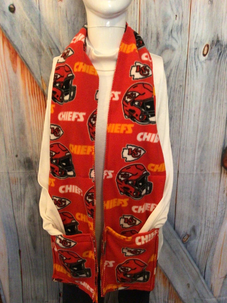 May include: Red fleece scarf with a pocket and a repeating pattern of the Kansas City Chiefs logo and the word "Chiefs".