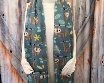 May include: Teal fleece scarf with a repeating pattern of sloths hanging from branches. The scarf has two pockets and is displayed on a mannequin. Yellow star and leaf accents complete the design.
