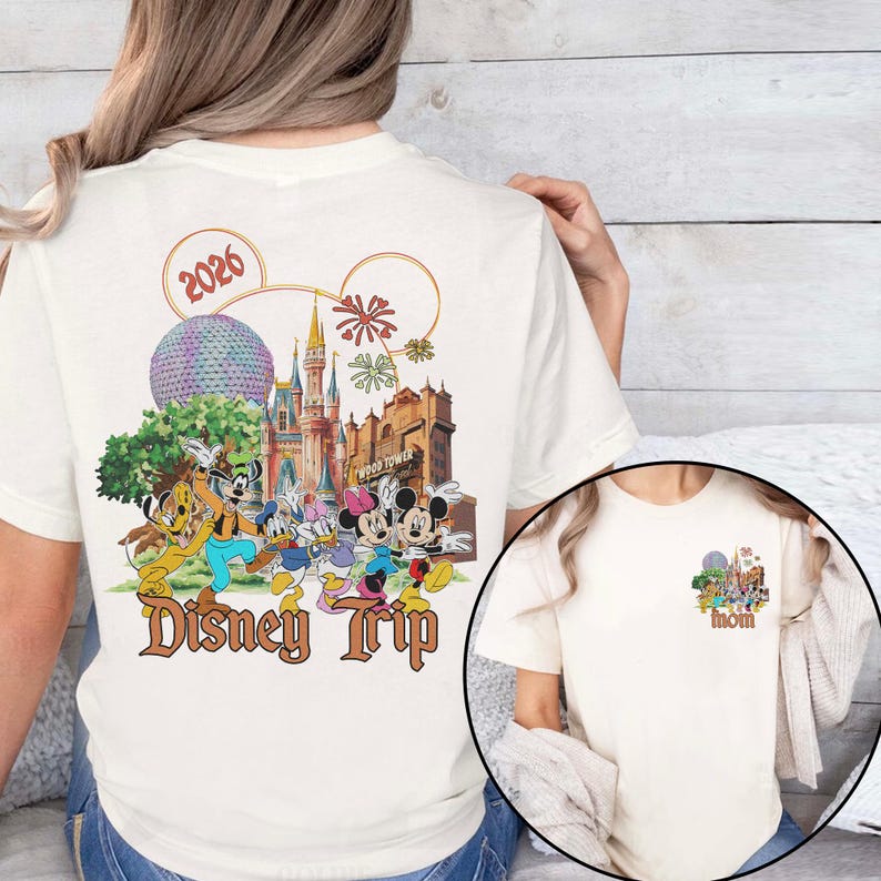May include: Cream-colored t-shirt featuring a colorful Disney Trip graphic on the back, including Mickey and Minnie Mouse, Donald Duck, and Goofy. The design incorporates the year 2026, a castle, and the text "Disney Trip."