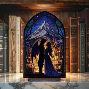 May include: A stained glass panel depicting a couple in silhouette with a mountain and city backdrop. The panel features a dark blue night sky with stars and a mountain range. The couple is in front of a city with illuminated windows. The panel is set against a backdrop of books.
