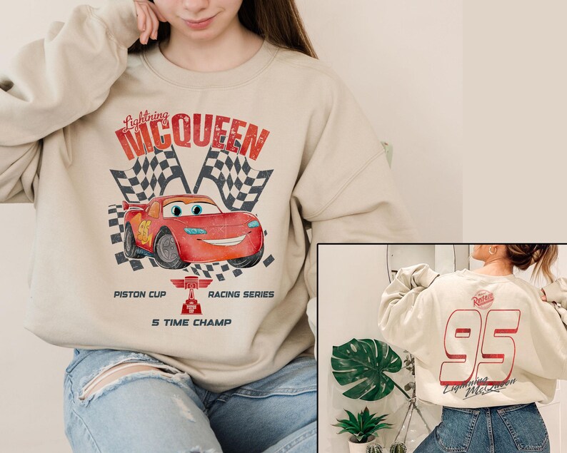 May include: Beige sweatshirt featuring a graphic of Lightning McQueen from the movie Cars, with checkered flags and text. The back of the sweatshirt displays the number 95 in red. The sweatshirt is a crew neck style.