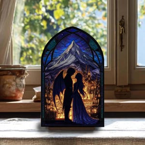 May include: A stained glass-style night light featuring a romantic scene. A silhouetted couple stands before a mountain and a city, under a starry sky. The artwork is framed in black and set on a wooden base, creating a warm, inviting glow.