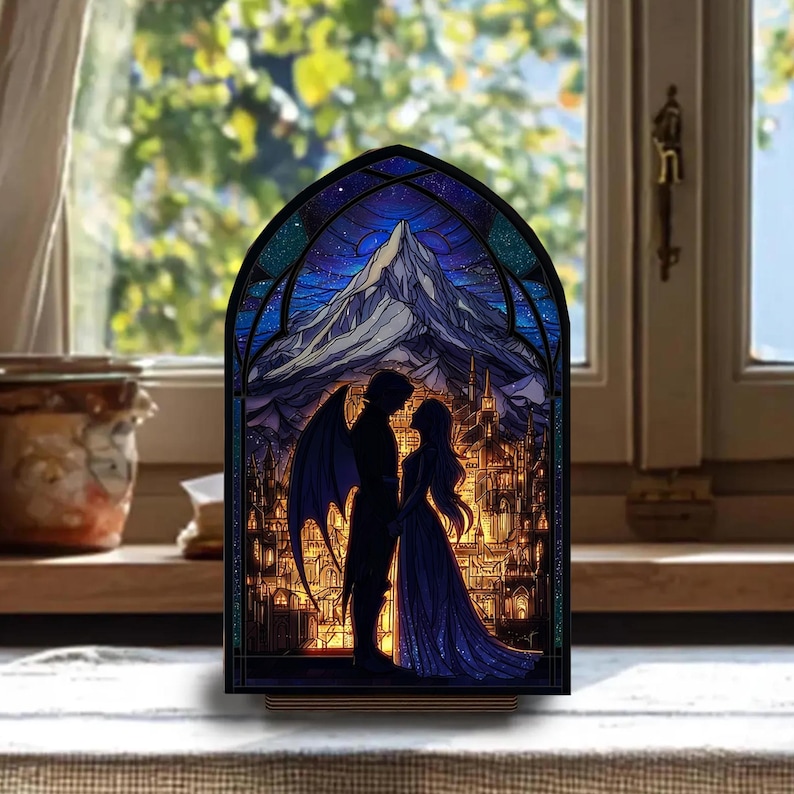 May include: A stained glass-style night light featuring a romantic scene. A silhouetted couple stands before a mountain and a city, under a starry sky. The artwork is framed in black and set on a wooden base, creating a warm, inviting glow.