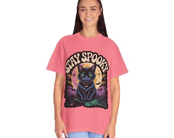 May include: A coral-colored t-shirt featuring a graphic of a black cat with green eyes, a collar, and the text "Stay Spooky." The cat is set against a full moon, bats, and a graveyard scene.