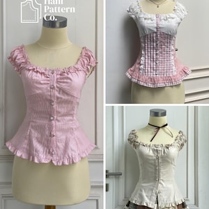 May include: Three fitted tops displayed on mannequins. One is solid light pink with a ruffled neckline and hem. Another is white and pink gingham with a button-down front and ruffles. The third is cream-colored with a button-down front.