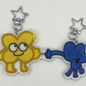 Puede incluir: Dos llaveros de personajes de dibujos animados. Uno es amarillo y tiene forma de X, el otro es azul y tiene forma del número cuatro. Ambos tienen cierres plateados en forma de estrella.