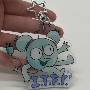 May include: A clear acrylic keychain featuring a cartoon character in shades of blue with the text "I.T.F.T." The keychain has a silver star-shaped clasp and a silver ring.
