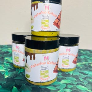 May include: A stack of four jars of pistachio kataifi spread. Each jar has a black lid and a white label with the product name, a jar graphic, and the text "8 oz 225 gms". The spread is a light green color.