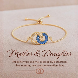 May include: A gold-tone adjustable bracelet featuring two interlocking circles, one encrusted with clear stones and the other with blue baguette stones. Text reads: Mother & Daughter. Made for you and me, marked by birthstones. Two months, two souls, one endless love.