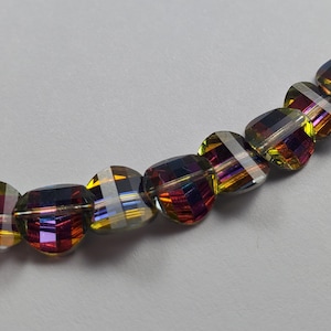 May include: A string of iridescent, faceted beads. The beads are oval-shaped with a flat top and bottom. The colours shift from yellow to purple to blue, with a silver-coloured line across each bead. The beads are strung on a clear string.