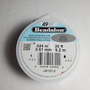 Pode incluir: Um carretel de fio para contas Beadalon, com 0,61 mm de diâmetro e 9,2 m de comprimento. O rótulo inclui texto em inglês, francês e espanhol, com a palavra "Bright" em destaque. O carretel é branco com um design azul claro e preto.