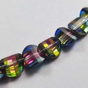 Peut inclure: Gros plan sur un fil de perles irisées et facettées. Les perles présentent un mélange de couleurs, notamment le bleu, le vert, le jaune et le rose, avec une surface brillante et réfléchissante. Les perles sont de forme ovale et enfilées.