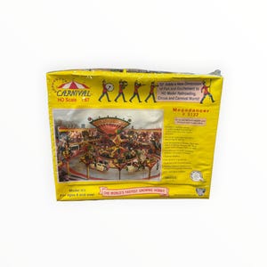 May include: A yellow cardboard box for a Carnival HO scale 1:87 model kit, Megadancer #5132. The front features a graphic of a carnival ride, text detailing the kit contents, and illustrations of marching band figures in red uniforms.
