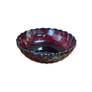 May include: A ruby-red glass bowl with a scalloped rim. The bowl has a textured surface and a dark interior. The bowl is likely for serving or display.