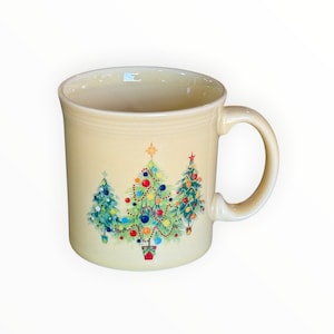 May include: Cream-colored ceramic mug featuring three decorated Christmas trees. The trees are adorned with colorful ornaments, garlands, and topped with stars. The mug has a curved handle and a smooth, glossy finish, perfect for holiday beverages.