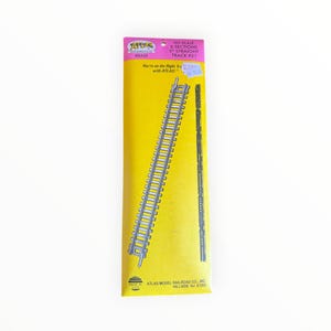 May include: A package of Atlas HO scale 6-section 9-inch straight brass model train track. The yellow packaging features the Atlas logo, the text 'You're on the Right Track with ATLAS!', and the Atlas Model Railroad Co. Hillside NJ 07205 address.