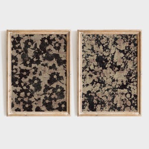 May include: Two framed floral art prints. Each print features a dark floral pattern on a beige background. The frames are a light wood colour. The floral design has a vintage, abstract style.